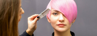 女理发师梳理染色粉红色的短头发年轻的女人黑暗墙