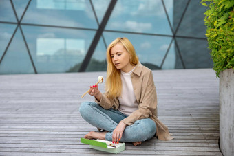 年轻的美丽的金发碧眼的女人吃寿司在户外木阳台现代建筑城市美味的食物女孩午餐打破支出时间吃亚洲食物城市生活