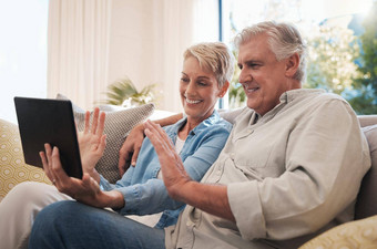 高级夫妇数字平板电脑波视频调用会说话的沙发生活房间视频会议上了年纪的男人。女人微笑快乐谈话在线虚拟闲谈，聊天