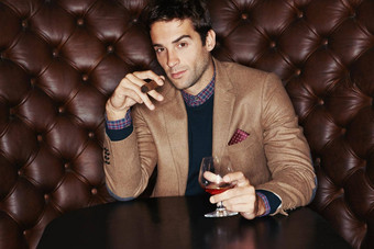 爱好雪茄威士忌肖像英俊的年轻的男人。喝吸烟雪茄俱乐部