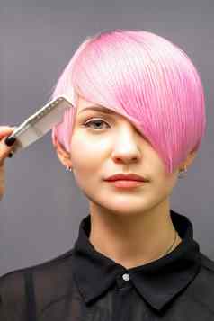 女理发师梳理染色粉红色的短头发年轻的女人黑暗墙
