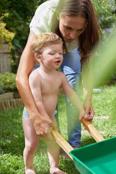 学习园艺婴儿男孩推玩具轮巴罗妈妈。帮助