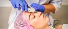 年轻的高加索人女人接收面部皮肤清洁超声波美容脸设备医疗沙龙