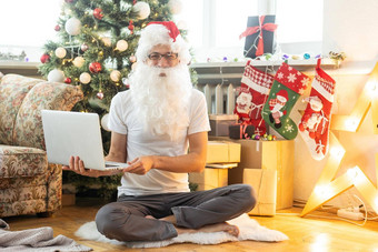 快乐圣诞老人老人西装坐着扶手椅移动PC圣诞节夏娃在线电子商务商店圣诞节假期在线出售概念背景圣诞节树花环墙