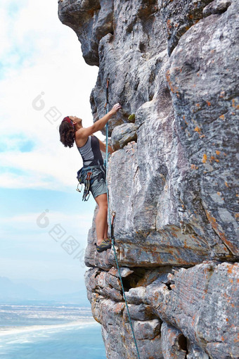 肾上腺素推<strong>峰会</strong>年轻的女人攀爬岩石脸框架蓝色的天空