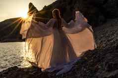 神秘的女轮廓长辫子站海海滩山的观点日落射线发光女人抛出长白色衣服神圣的日落