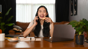 微笑年轻的亚洲女人坐着前面移动PC首页办公室会说话的移动电话
