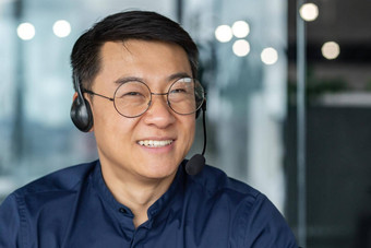 肖像男人。<strong>耳机</strong>视频调用亚洲工人微笑相机科技客户支持服务商人工作内部现代办公室建筑