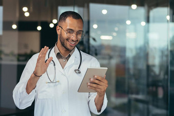 快乐的拉美裔医生医疗白色外套听诊器平板电脑电脑视频调用在线咨询病人男人。工作内部诊所办公室建筑