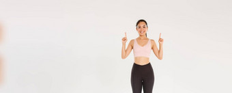 体育运动健身房健康的身体概念完整的长度快乐的微笑可爱的健身女孩指出手指显示锻炼设备广告买会员培训