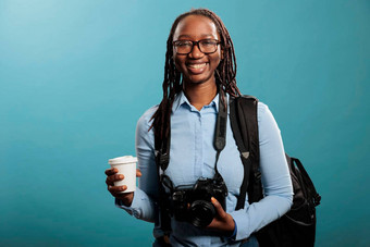 微笑衷心地年轻的成人女人数码单反相机相机设备杯咖啡站蓝色的背景