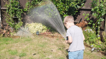 有趣的男孩浇水草坪上植物花园住房后院可爱的孩子玩灌溉软管热阳光明媚的夏天在户外孩子们做家务活动孩子们童年