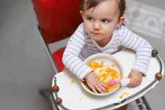 位饥饿的可爱的婴儿坐着高椅子吃