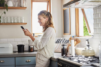 成熟的女人阅读电话新闻社会媒体通知移动应用程序澳大利亚厨房首页快乐夫人打字智能手机在线社会网络网络技术连接公寓