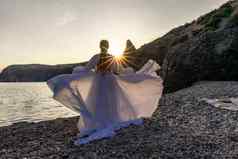 神秘的女轮廓长辫子站海海滩山的观点日落射线发光女人抛出长白色衣服神圣的日落