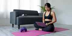 女人移动PC锻炼首页女运动服装坐着地板上看锻炼视频锻炼