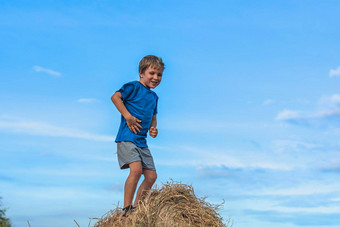 男孩微笑玩跳舞鬼脸显示蓝色的t恤站干草堆包干草清晰的天空阳光明媚的一天平衡培训概念快乐童年孩子们在户外清洁空气关闭自然