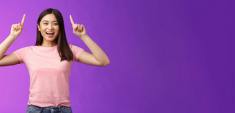 有魅力的好看的活泼的微笑亚洲女孩介绍产品指出手指前广告咧着嘴笑露出牙齿的兴奋告诉好新闻分享链接紫色的背景