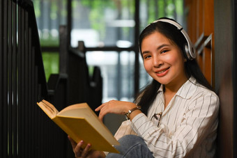 微笑亚洲女人穿耳机阅读书图书馆人知识教育概念