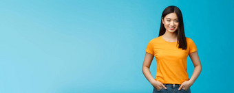<strong>自信自信</strong>的微笑亚洲女人站蓝色的背景相机持有手牛仔裤口袋表达<strong>自信</strong>的氛围享受积极的结果护肤品程序穿黄色的t恤