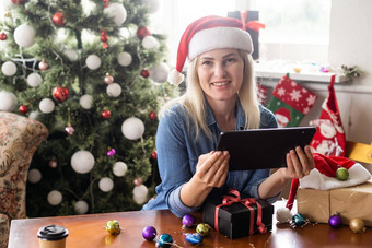 年轻的女人背景圣诞节树礼物平板电脑视频调用视频闲谈，聊天朋友家庭圣诞节在线假期保持首页假期