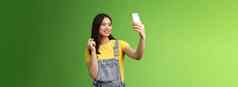 魅力温柔的十几岁的亚洲女采取自拍检查发型智能手机前面相机拍摄记录视频消息帖子在线微笑可爱的绿色背景