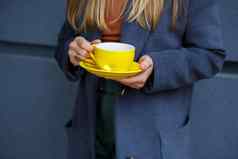 年轻的美丽的金发女郎女人灰色的外套饮料热茶黄色的杯冷秋天一天美味的温暖的喝阳台咖啡馆