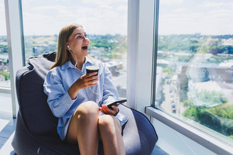 年轻的经理女人耳机会说话的电话喝咖啡坐着现代共同办公空间自由女孩工作远程在线