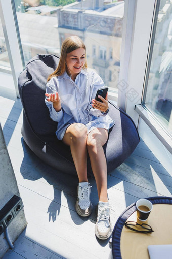 年轻的女孩听音乐耳机手表移动电话现代女人生活方式概念年轻的女人坐着共同办公空间办公室室内