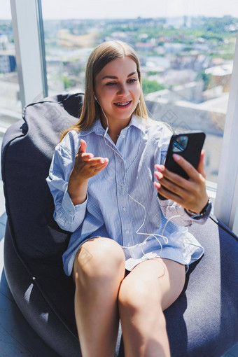 年轻的女孩听音乐耳机手表移动电话现代女人生活方式概念年轻的女人坐着共同办公空间办公室室内