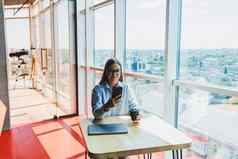 成功的女人移动PC咖啡馆喝咖啡年轻的微笑女人眼镜坐在表格窗口电话自由远程工作现代女生活方式