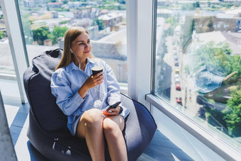 年轻的经理女人耳机会说话的电话喝咖啡坐着现代共同办公空间自由女孩工作远程在线