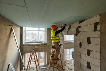 专业工人站梯使测量磁带测量安装干墙天花板高层建筑建设