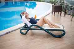 美丽的年轻的女人泳衣白色衬衫坐在太阳懒人池按摩身体防晒霜夏天皮肤护理保护皮肤燃烧