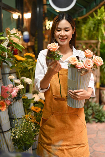 积极的年轻的女人小业务企业家穿围裙持有花束粉红色的玫瑰站前面花商店