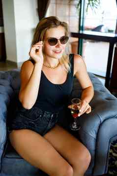 美丽的年轻的女人坐在软扶手椅酒店游说团体玻璃香槟假期穿太阳镜微笑脸假期概念