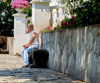 上了年纪的男人。休息板凳上白色古董石头墙城市公园