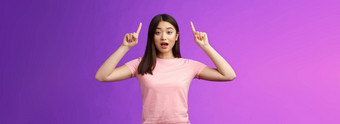 兴奋可爱的惊讶亚洲女孩粉红色的t恤告诉太棒了新闻指出提高了手指前广告开放口惊讶激动站蓝色的背景