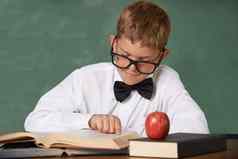 爱读年轻的男孩穿眼镜蝴蝶结集中阅读红色的苹果表格前面