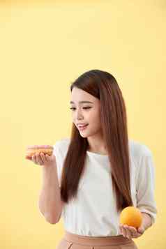 肖像微笑年轻的亚洲女人选择甜甜圈橙色孤立的黄色的背景