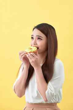 关闭肖像满意漂亮的女孩吃甜甜圈孤立的黄色的背景