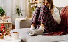 舒适的女人腿针织冬天温暖的袜子毛衣网纹格子喝热可可咖啡杯子休息沙发上首页圣诞节假期蜡烛装饰饼干
