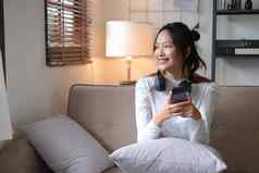 快乐快乐的年轻的亚洲女选择音乐播放列表移动电话听音乐耳机放松生活房间