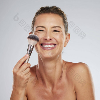美化妆护肤品刷成熟的女人应用化妆品脸工作室灰色背景头肖像女脸红的人美丽的快乐健康的