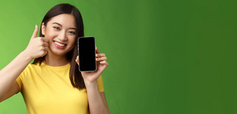 特写镜头满意可爱的亚洲女孩给积极的反馈翘拇指显示智能手机屏幕介绍太棒了应用程序推荐好应用程序吹牛打分数游戏