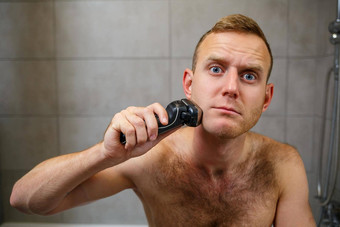 男人。刮胡子脸电剃须刀前面镜子皮肤刺激浴过程