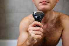 男人。刮胡子脸电剃须刀前面镜子皮肤刺激浴过程