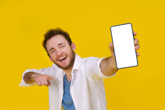 伟大的提供年轻的快乐男人。持有智能手机显示白色空屏幕令人兴奋的赢得孤立的黄色的背景庆祝成功产品放置空空间复制空间