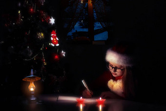 快乐圣诞节快乐假期孩子女孩圣诞老人老人帽写信圣诞老人老人梦想礼物背景一年树在室内问候卡高质量照片