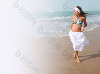 美丽的年轻的女人走光着脚桑迪海滩海洋风吹头发白色裙子